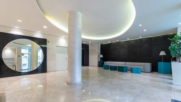 Eine geräumige Lobby mit Marmorboden, einer großen Säule in der Mitte, einem runden Spiegel, einer Couch und einer Zimmerpflanze.