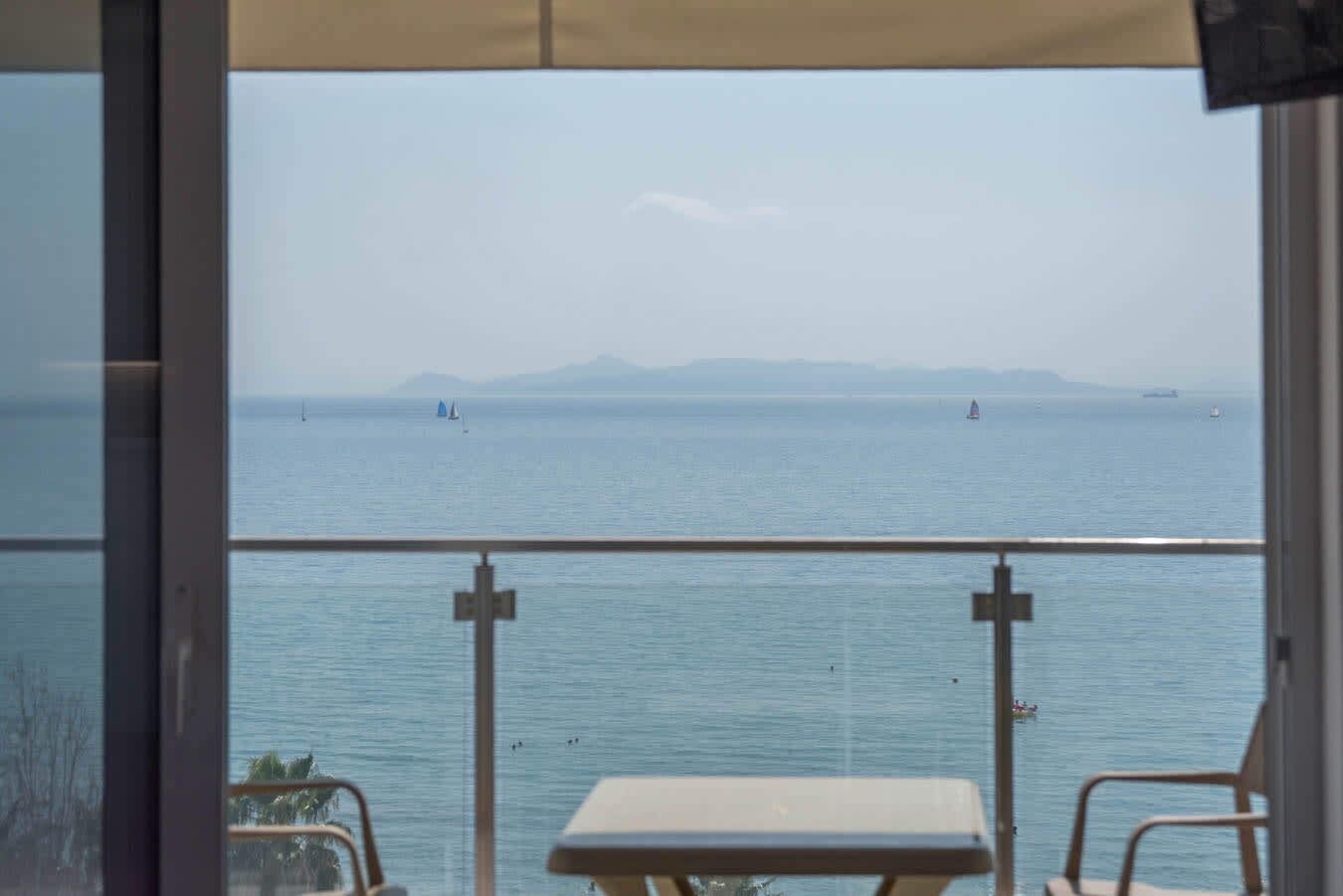 A balcony with a view of the sea, a table, and chairs.