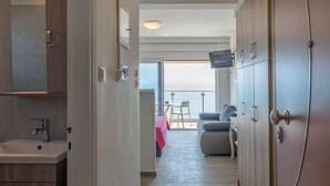 Un couloir étroit mène à un balcon où se trouvent un canapé et une table, ainsi qu’un téléviseur fixé au mur.