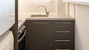 Une cuisine compacte équipée d’un lave-linge encastré, d’un évier et de placards.