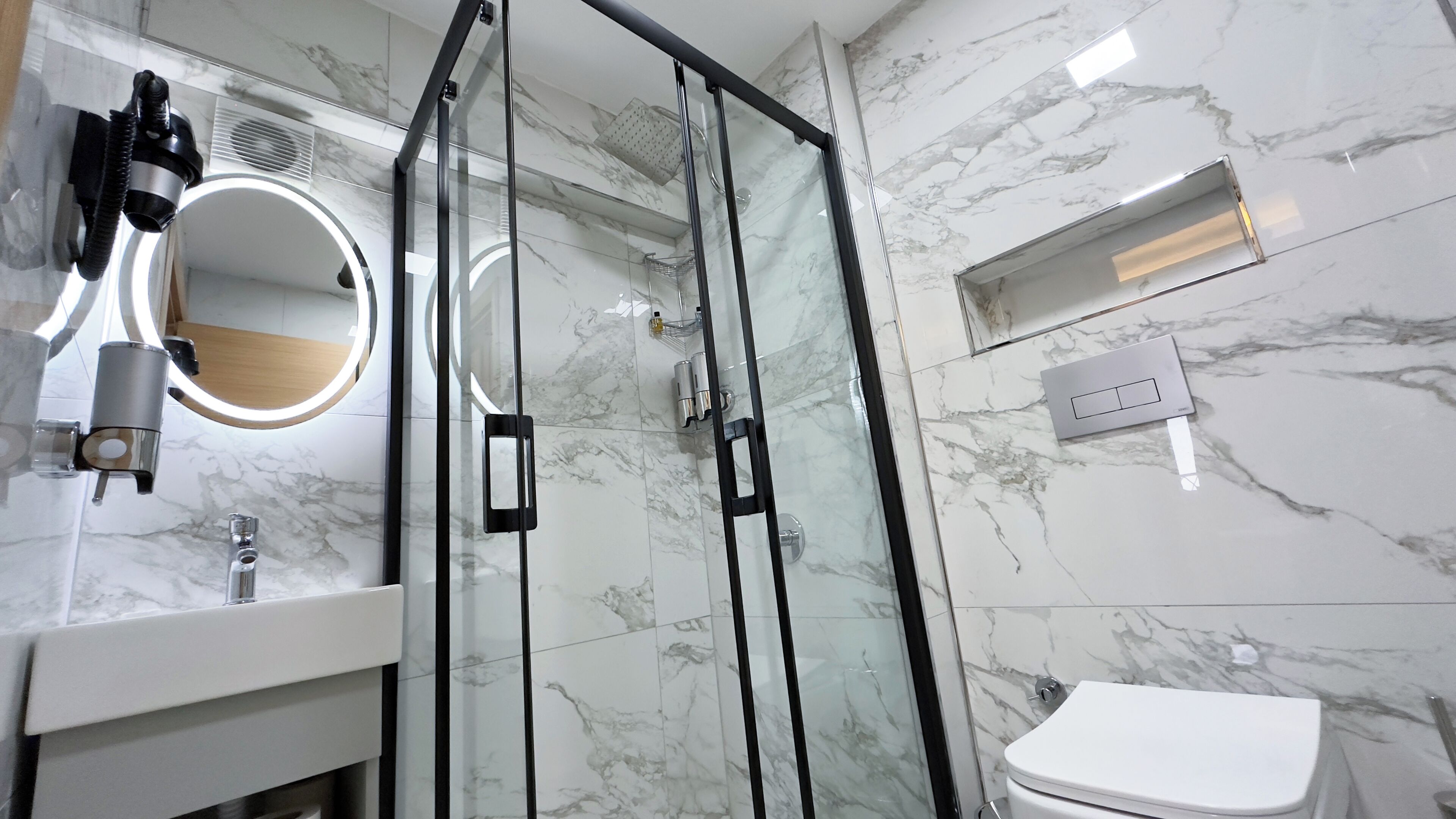 A modern bathroom with a glass-enclosed shower, a round mirror, and a toilet.