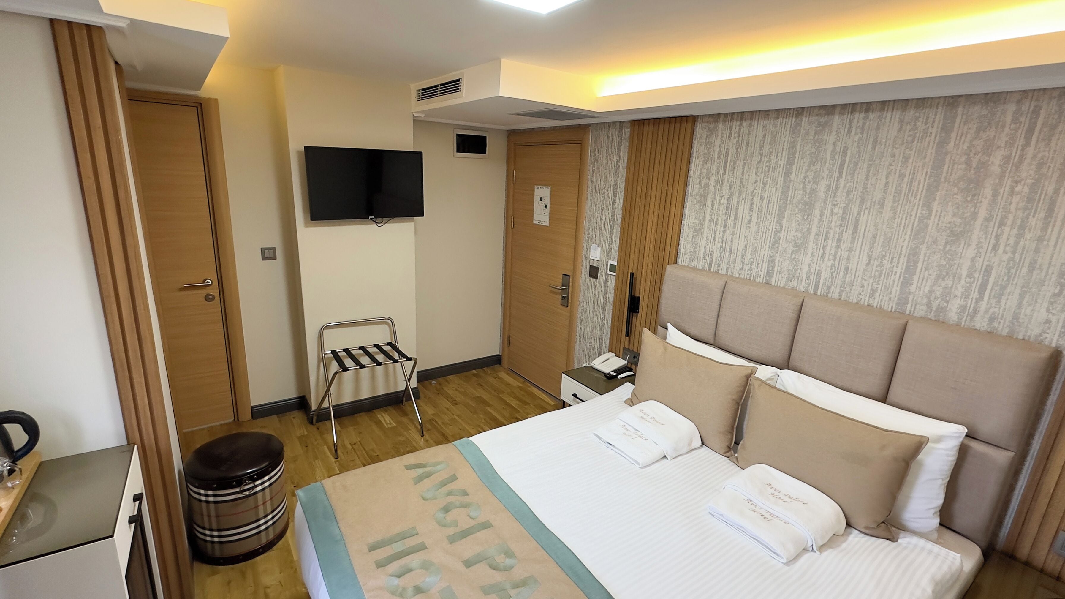 A hotel room with a bed, a television mounted on the wall, a small table with a telephone, and a waste bin.
