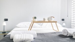 Een moderne hotelkamer met een opgemaakt bed, een nachtkastje met lamp en een tafeltje met decoratieve objecten.