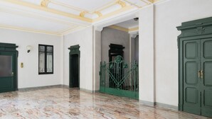 Een ruime kamer met een marmeren vloer, groene deuren en een decoratief plafond.