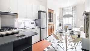 Een moderne keuken met witte kastjes, een roestvrijstalen koelkast en een eethoek met een glazen tafel en stoelen.