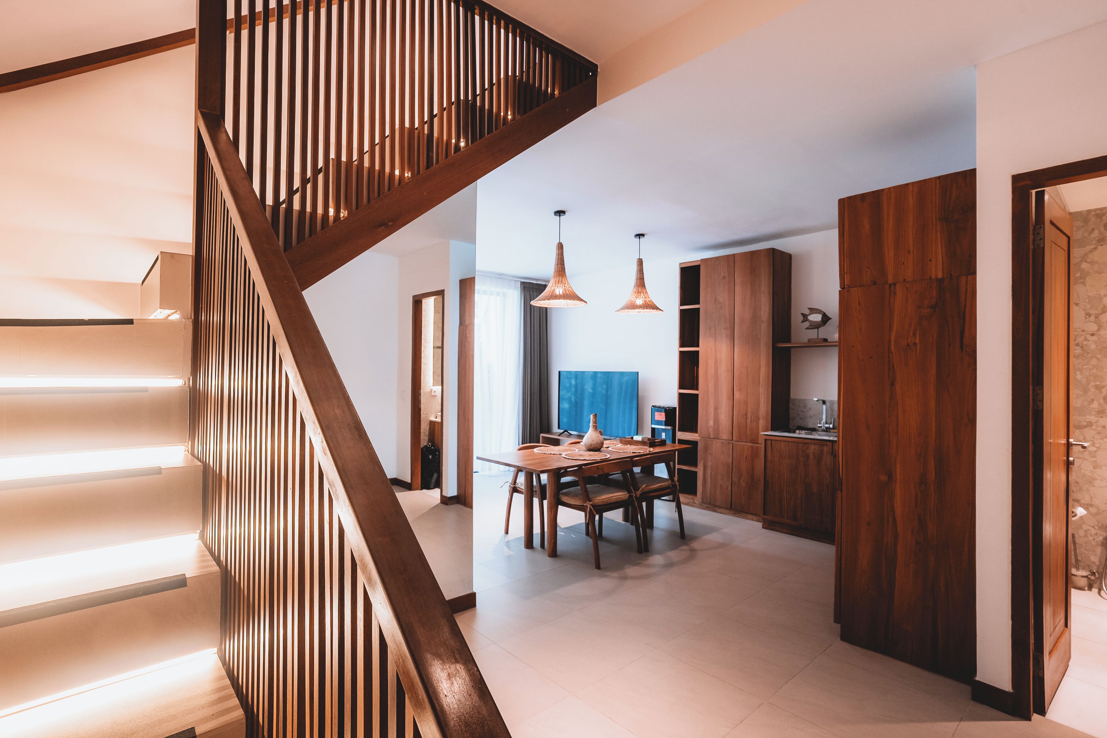 A modern kitchen with wooden cabinets, a dining table, and pendant lights.