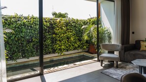 Una sala de estar moderna con una pared de vidrio, una piscina pequeña y diversas plantas de interior.