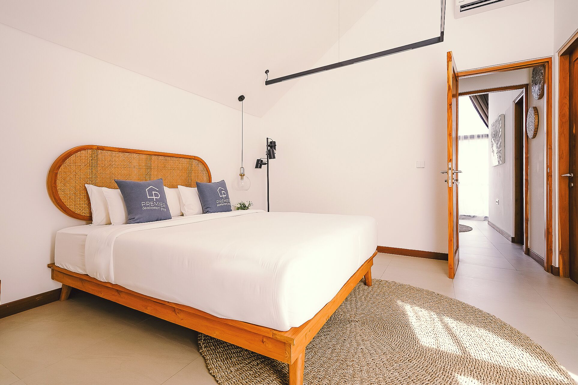 A bedroom with a wooden bed, white bedding, a rattan headboard, a floor lamp, and a view of the hallway.