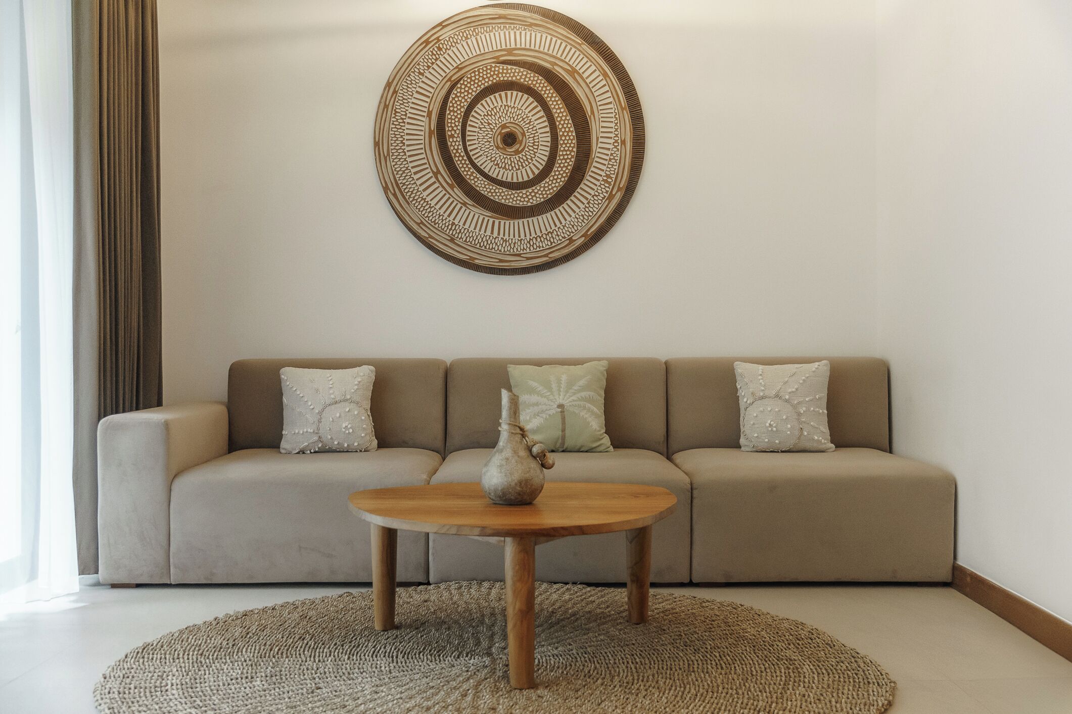 A living room with a beige sofa, a round coffee table, and a decorative wall piece.