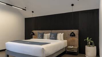 A modern bedroom with a large bed, two bedside lamps, a nightstand, a potted plant, and a wall-mounted light fixture.