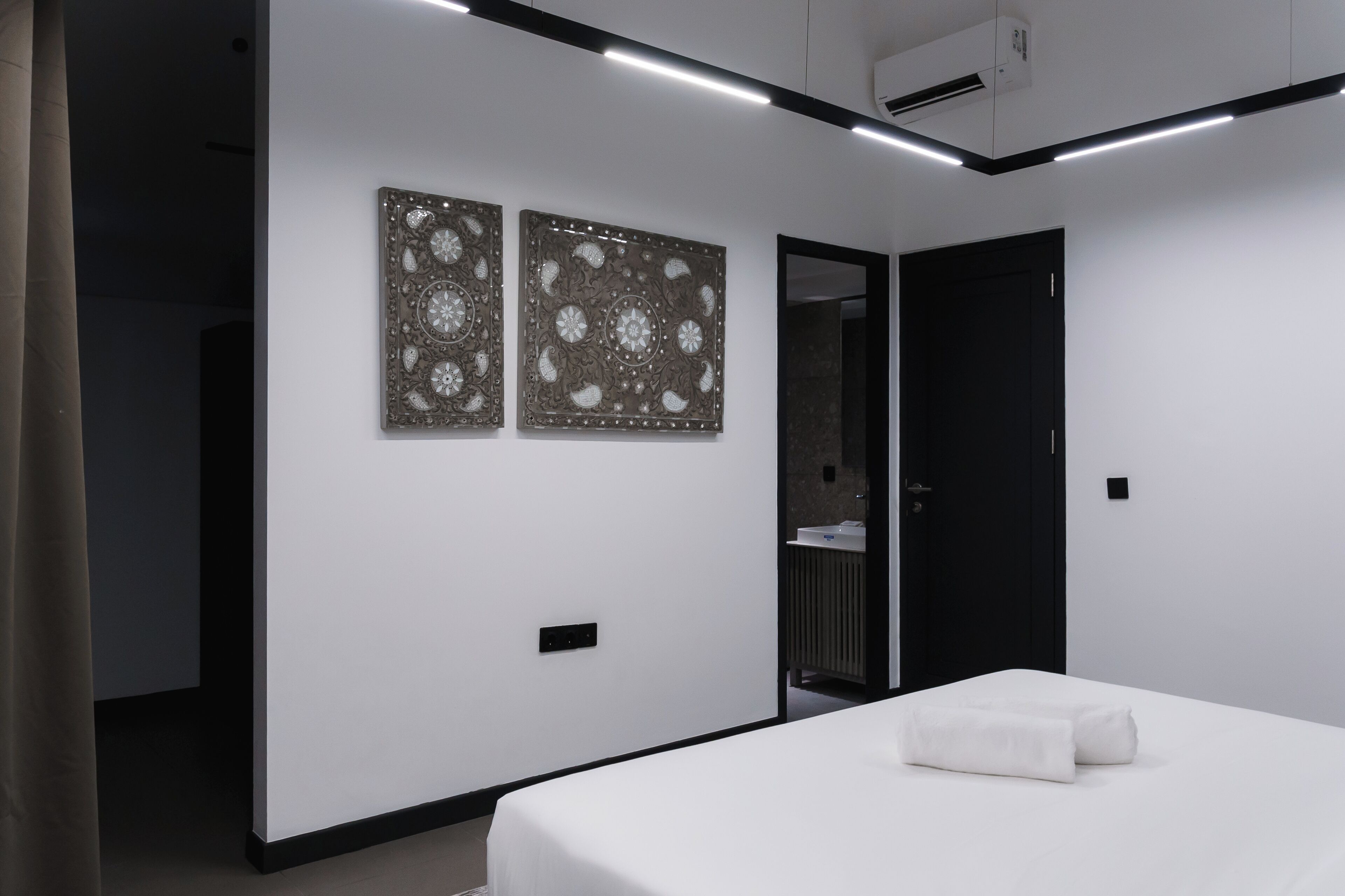 Ein modernes Hotelzimmer mit einem Bett, zwei Wandpaneelen zur Dekoration, einer Tür und einem sichtbaren Badezimmer.