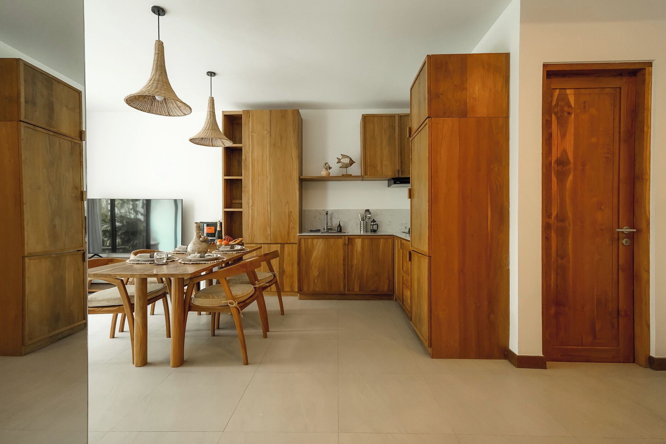 A modern kitchen with wooden cabinets, a dining table with chairs, and pendant lights.