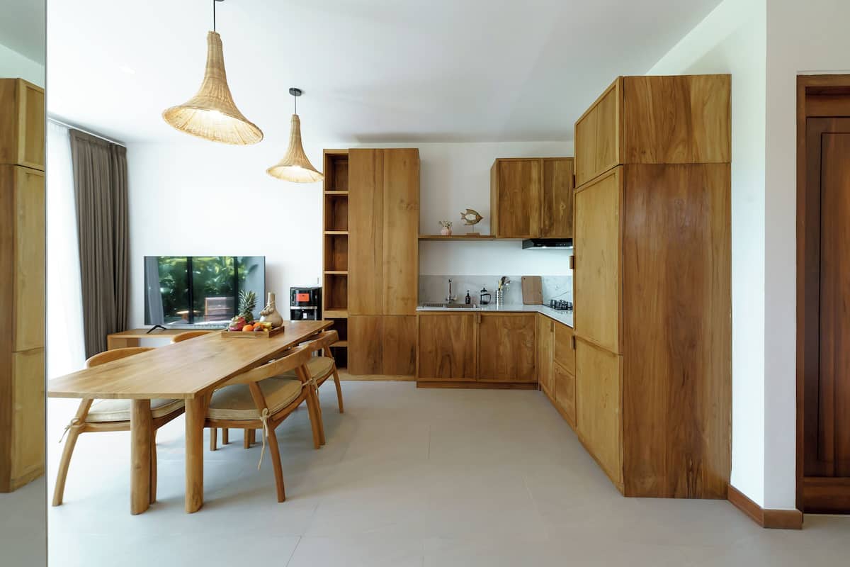 A modern kitchen with wooden cabinets, a dining table, and pendant lights.