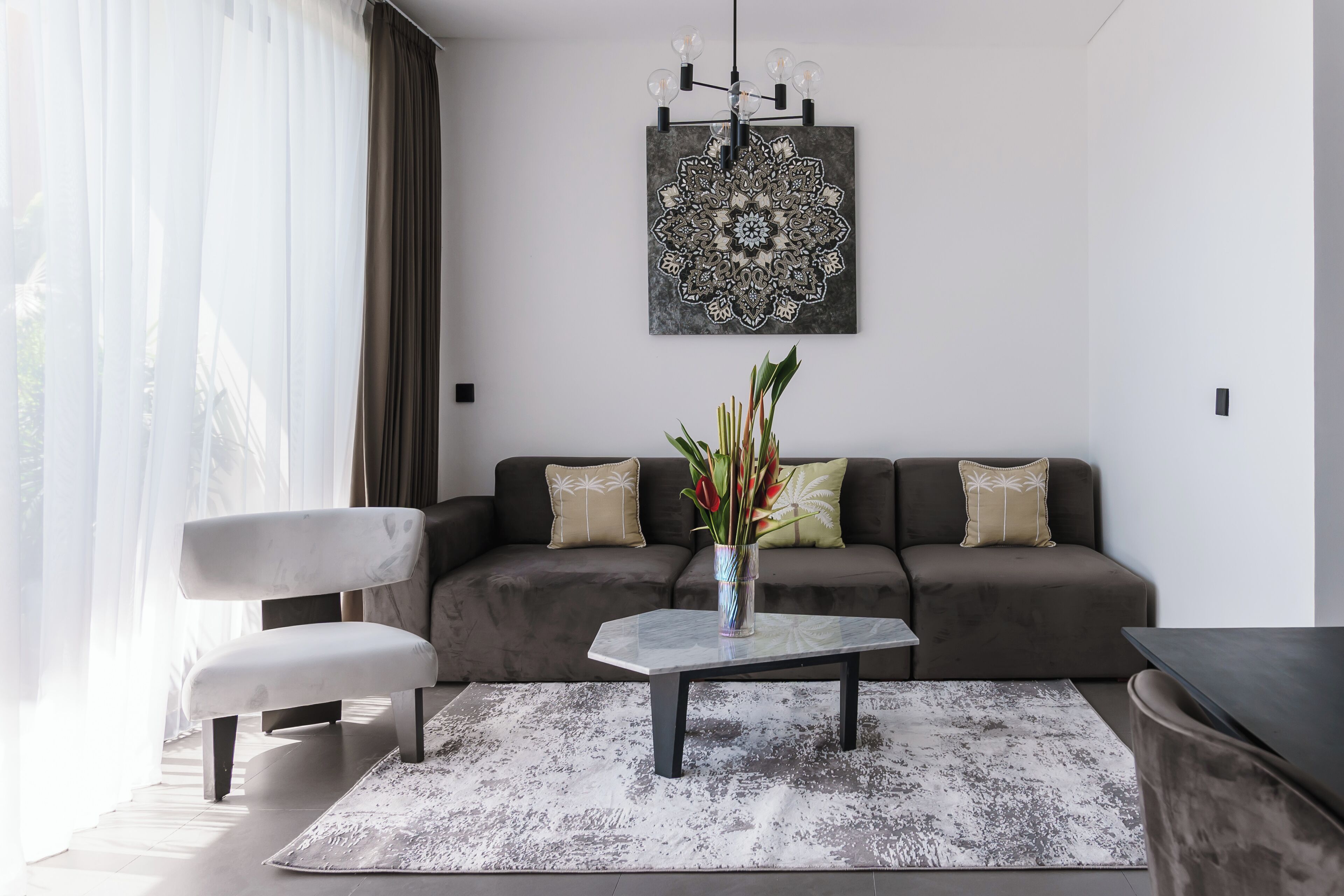 Una sala de estar moderna con un sofá gris, un sillón blanco, una mesa de centro y un jarrón decorativo.