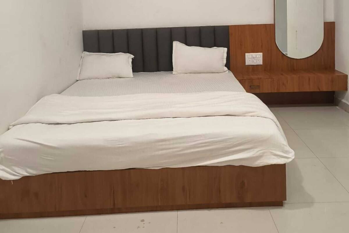 A bedroom with a wooden bed frame, white bedding, a grey headboard, and a round mirror on a wooden dresser.