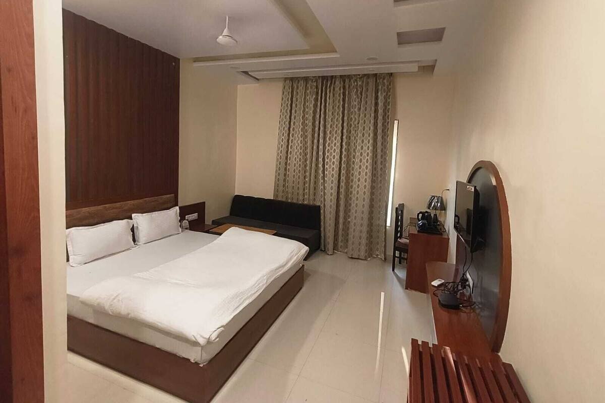 A hotel room with a large bed, a desk with a mirror, a television, and a window with curtains.