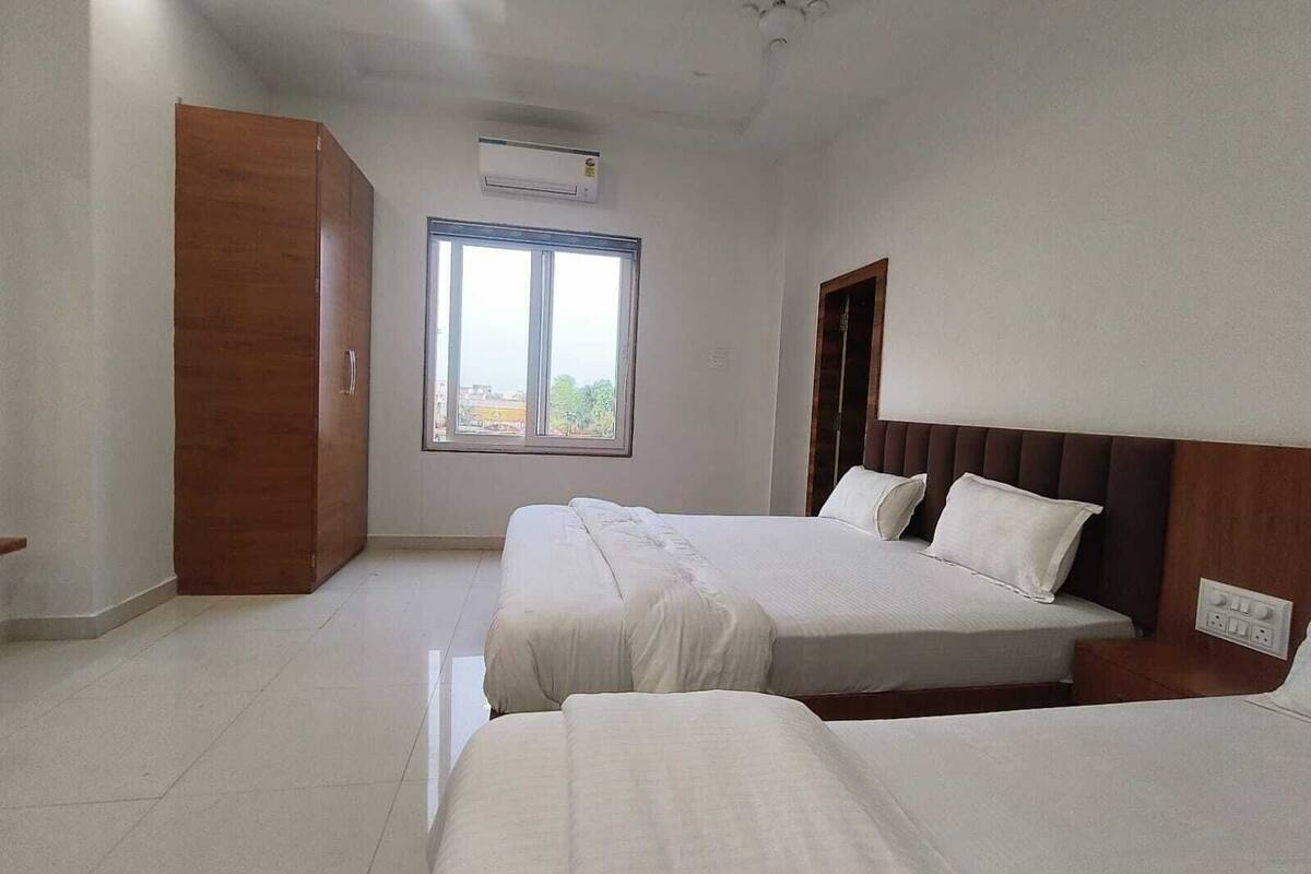 A hotel room with two beds, a window, an air conditioning unit, and a wooden wardrobe.
