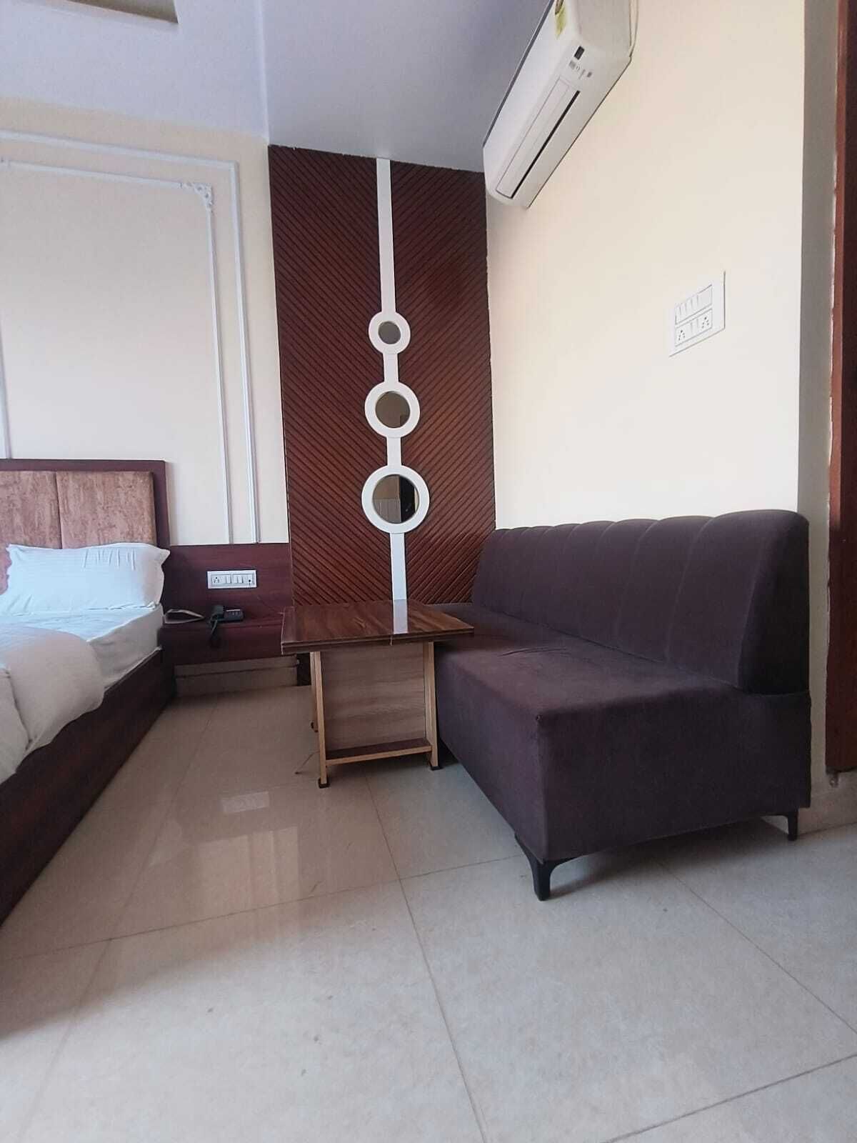 Una habitación de hotel con cama, una mesita de noche de madera, un sofá oscuro y un panel decorativo en la pared.