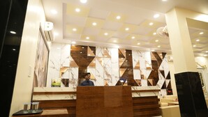 A hotel reception area with a marble counter, a wooden reception desk, and a ceiling with recessed lighting.