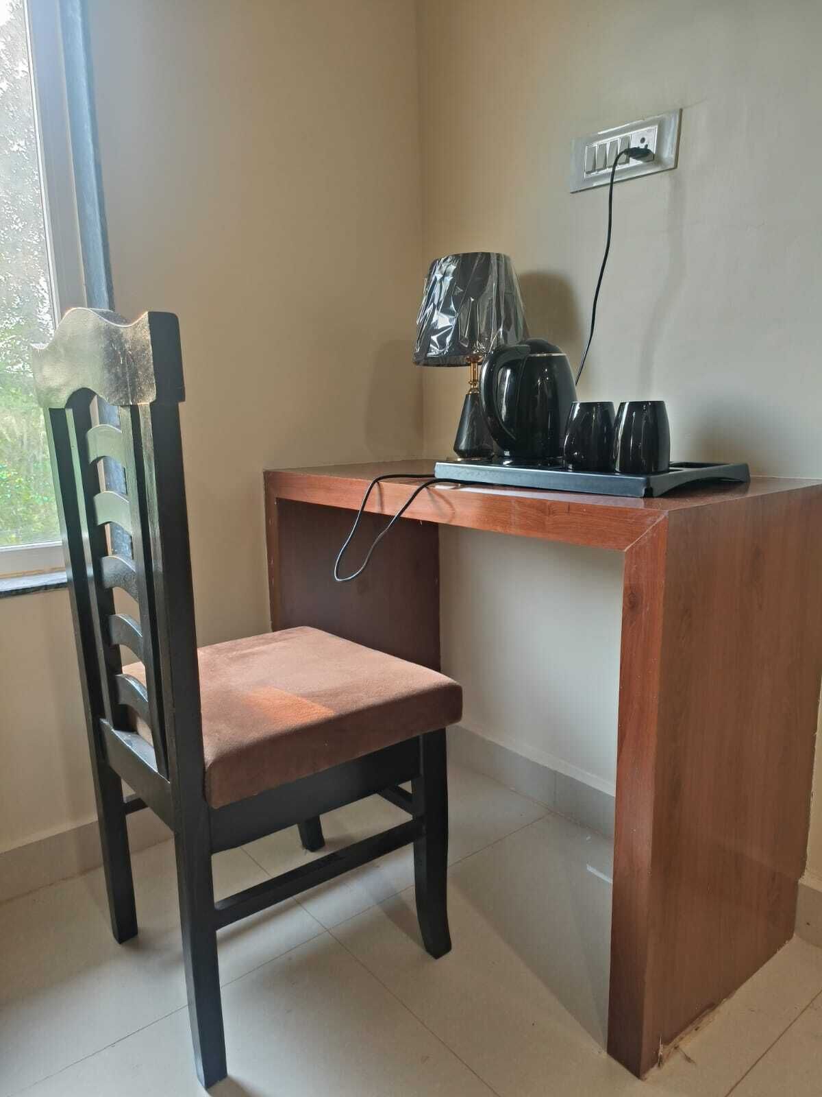 A small office space with a wooden desk, a chair, a lamp, and a kettle.