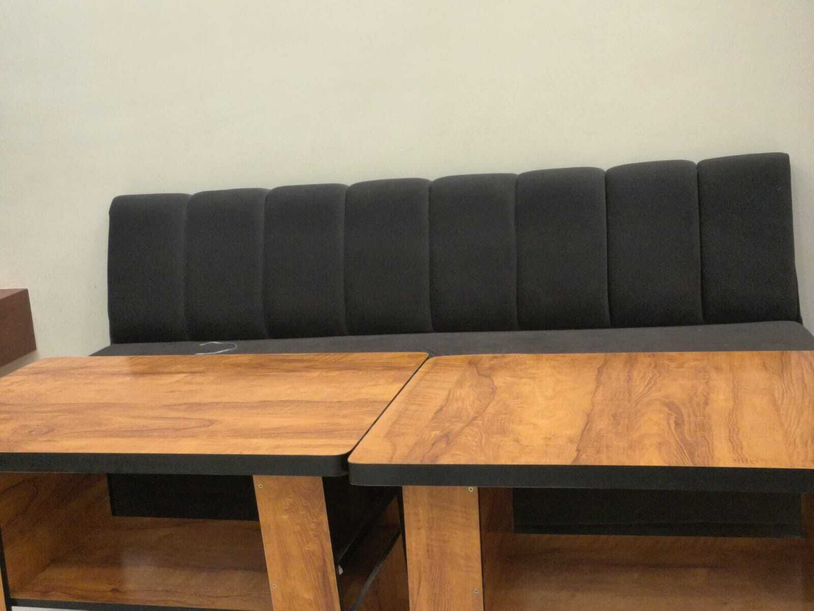 A modern room with a black sofa, two wooden tables, and a plain white wall.