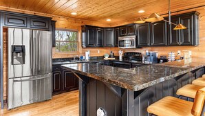 A modern kitchen with dark cabinets, stainless steel appliances, and a granite island with bar stools.