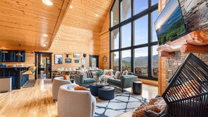 A spacious living area with a high ceiling, wooden walls, and large windows offering a scenic view.