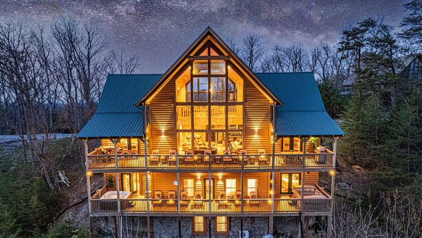 A large, multi-story log cabin with a prominent central tower, multiple balconies, and a wrap-around porch.