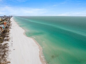 A coastal beach with a clear view of the ocean, a sandy shore, and buildings along the coastline.