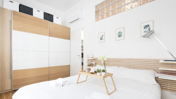 Una habitación de hotel moderna con una cama grande, un armario de madera y una mesita de noche con lámpara y adornos.