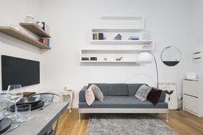 En moderne stue med en grå sofa, hvide reoler, et fladskærms-tv og et spiseområde med et bord dækket til to.