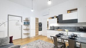 Una cocina moderna con armarios blancos, un comedor con una mesa preparada para dos comensales y un sofá gris en la sala.