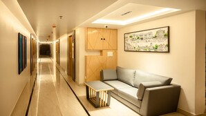 A modern hotel lobby with a long corridor, a sofa, a small table, and a framed artwork on the wall. - HOTEL LAKE VIEW (Baharampur)