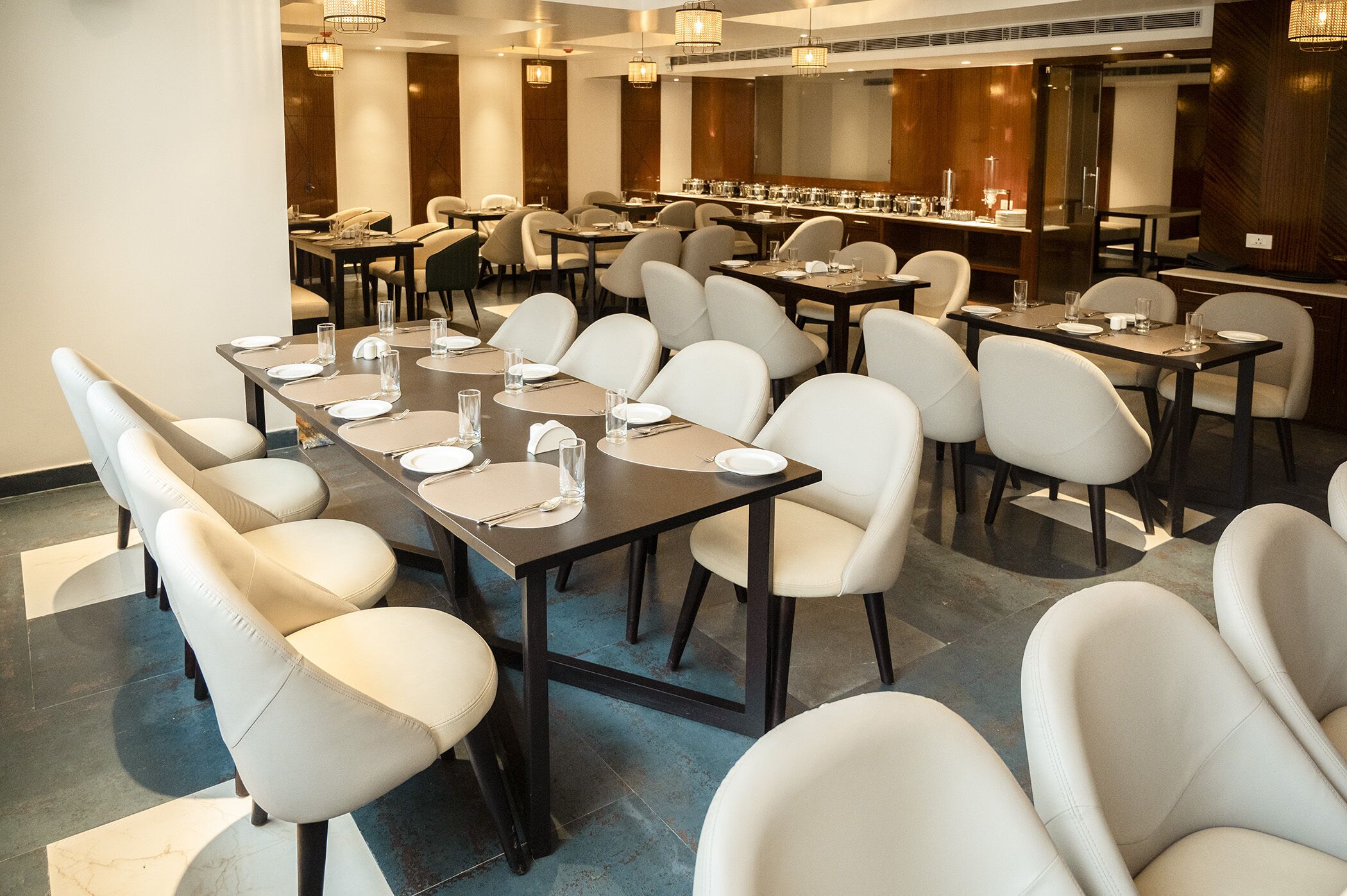 A spacious dining area with multiple tables and chairs, arranged in a modern setting with a neutral color palette.