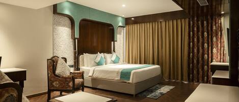 A hotel room with a bed, two armchairs, a small table, and a desk.