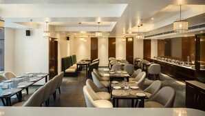 A modern dining area with multiple tables and chairs, a long counter with a bar, and pendant lighting. - HOTEL LAKE VIEW (Baharampur)