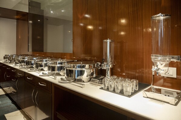 A buffet setup with multiple food stations, a coffee machine, and a glassware station.