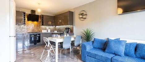 A modern kitchen with a dining area, a sofa, and a TV mounted on the wall.