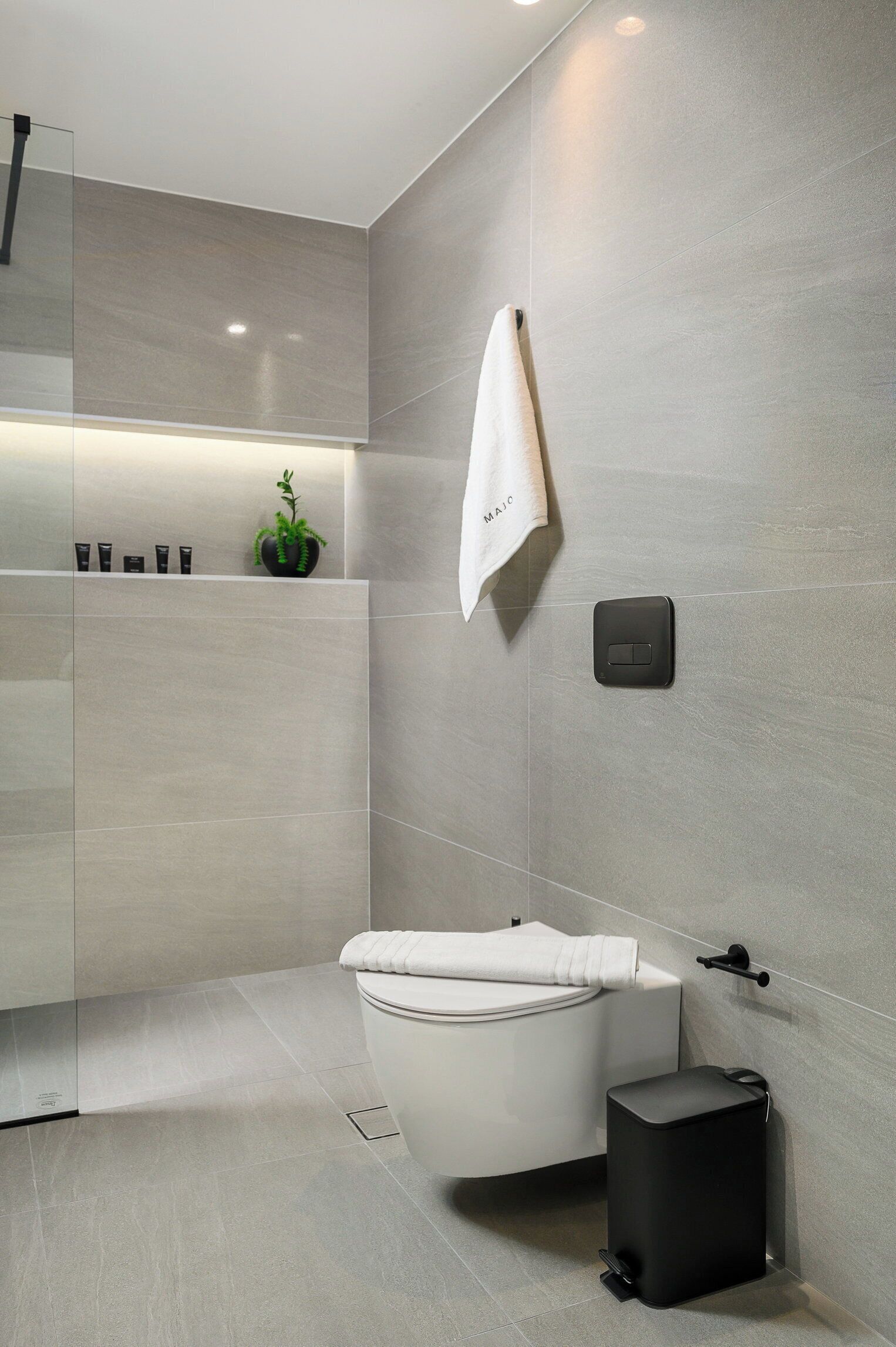 Ein modernes Badezimmer mit Toilette, schwarzem Mülleimer und einem Handtuch an einem Haken.