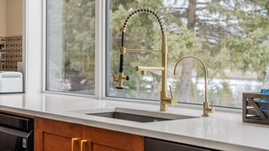 A kitchen with a modern stainless steel sink and a gold faucet. - Estate on Bow River 25 Min to  DT YYC 5BR w AC (Calgary)
