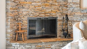 A stone fireplace with a large screen, a wooden chair, and a fireplace tool. - Estate on Bow River 25 Min to  DT YYC 5BR w AC (Calgary)
