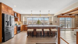 A modern kitchen with a large island, wooden cabinets, stainless steel appliances, and a view of the outdoors. - Estate on Bow River 25 Min to  DT YYC 5BR w AC (Calgary)