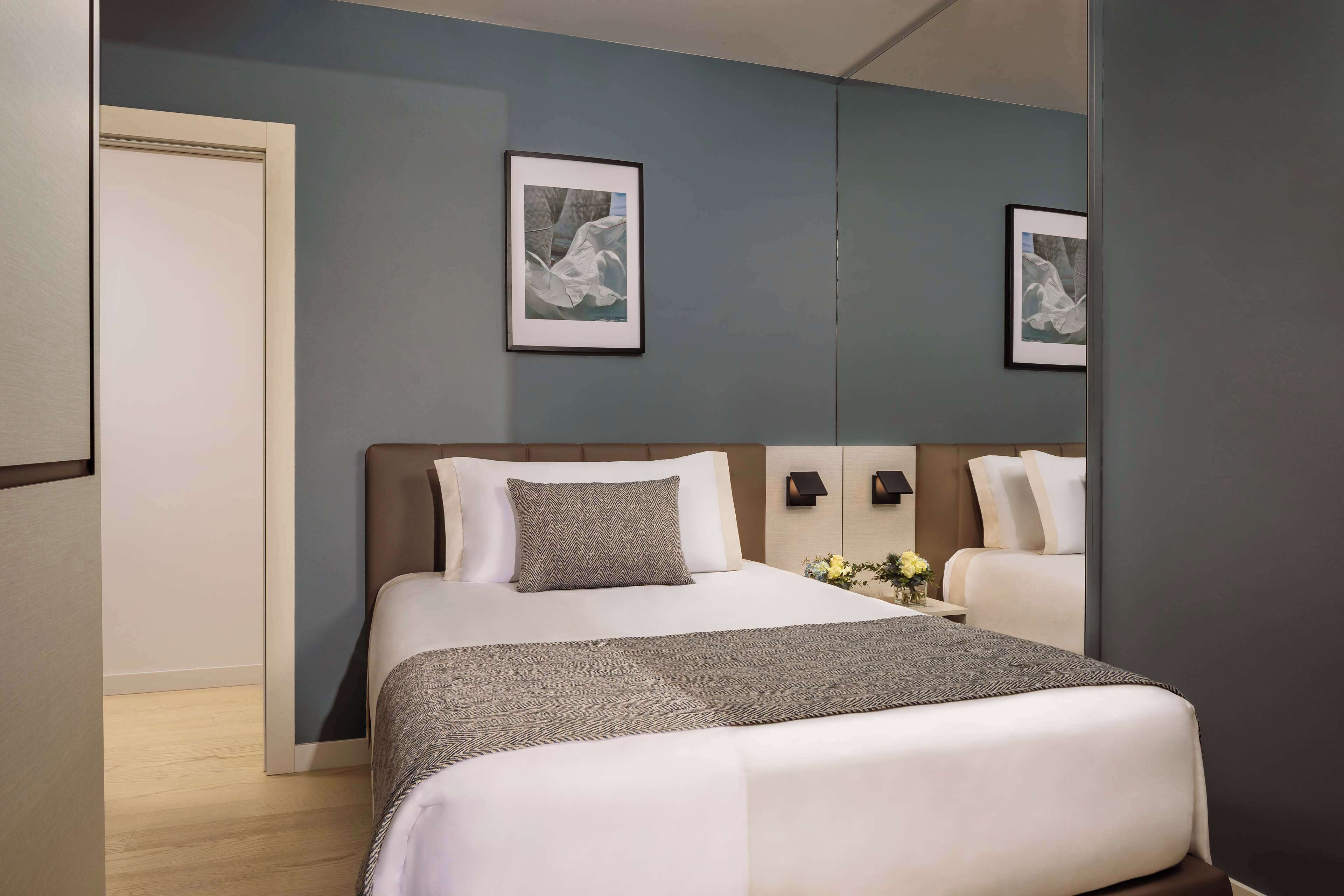 Une chambre d’hôtel avec un grand lit, une table de chevet avec une lampe et deux tableaux encadrés au mur.