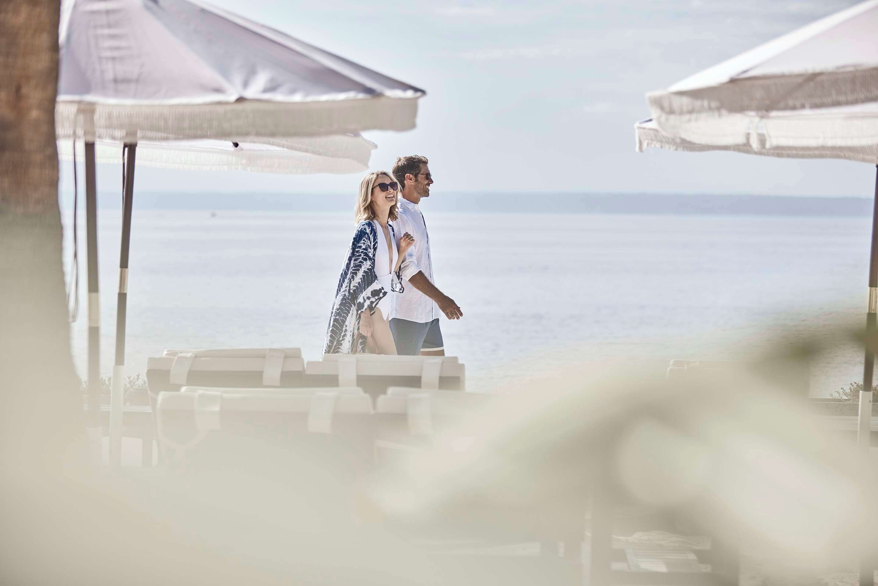 Una coppia cammina su una spiaggia con ombrelloni e lettini.