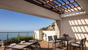 Une terrasse en bois avec une table et des chaises, une pergola et une vue sur la mer.