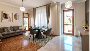 A modern living room with a dining area, wooden flooring, and a large window with curtains. - Cernobbio Garden View (Cernobbio)