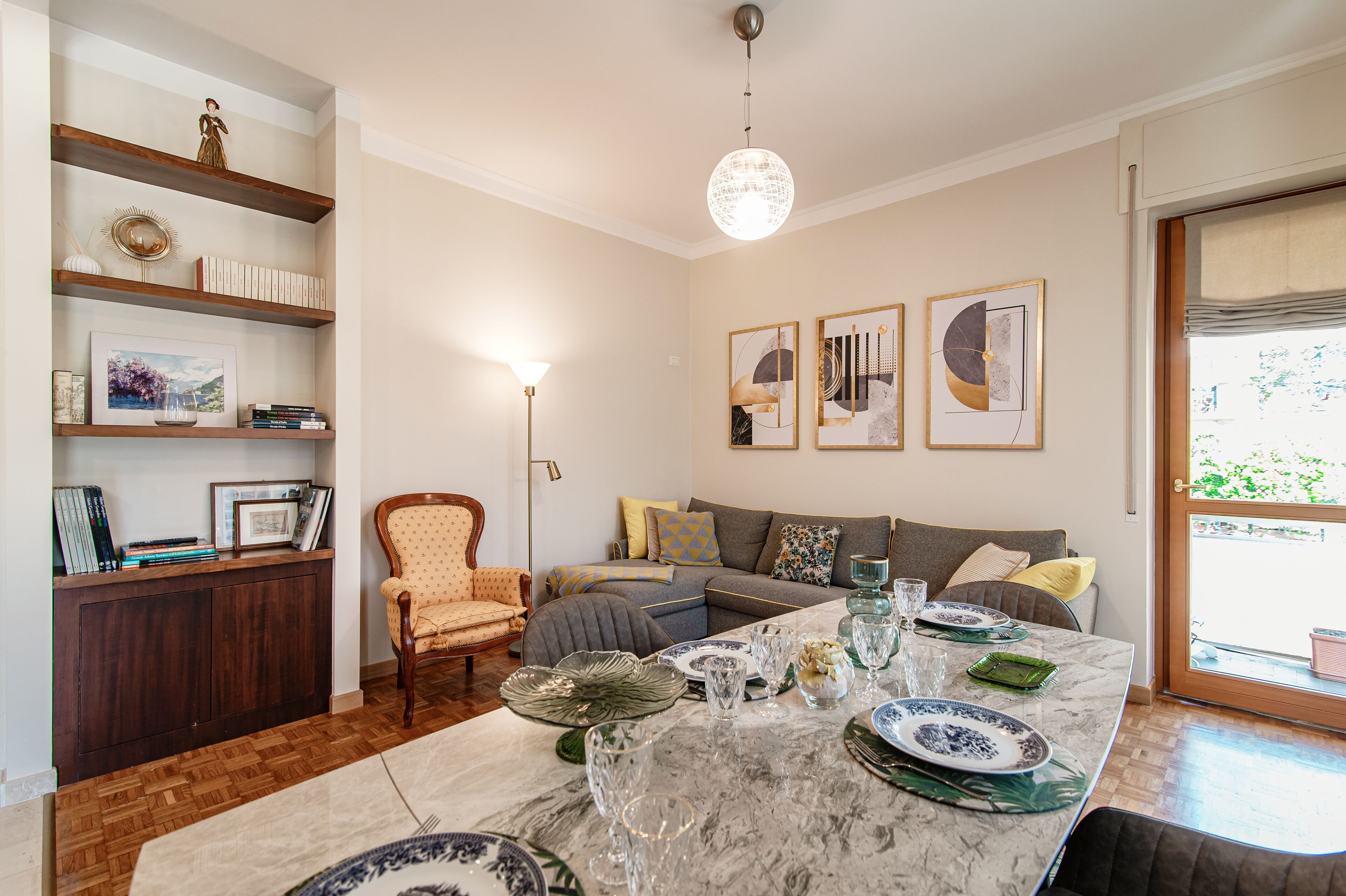A living room with a marble coffee table, a sofa, a bookshelf, and a dining area with plates and glasses.