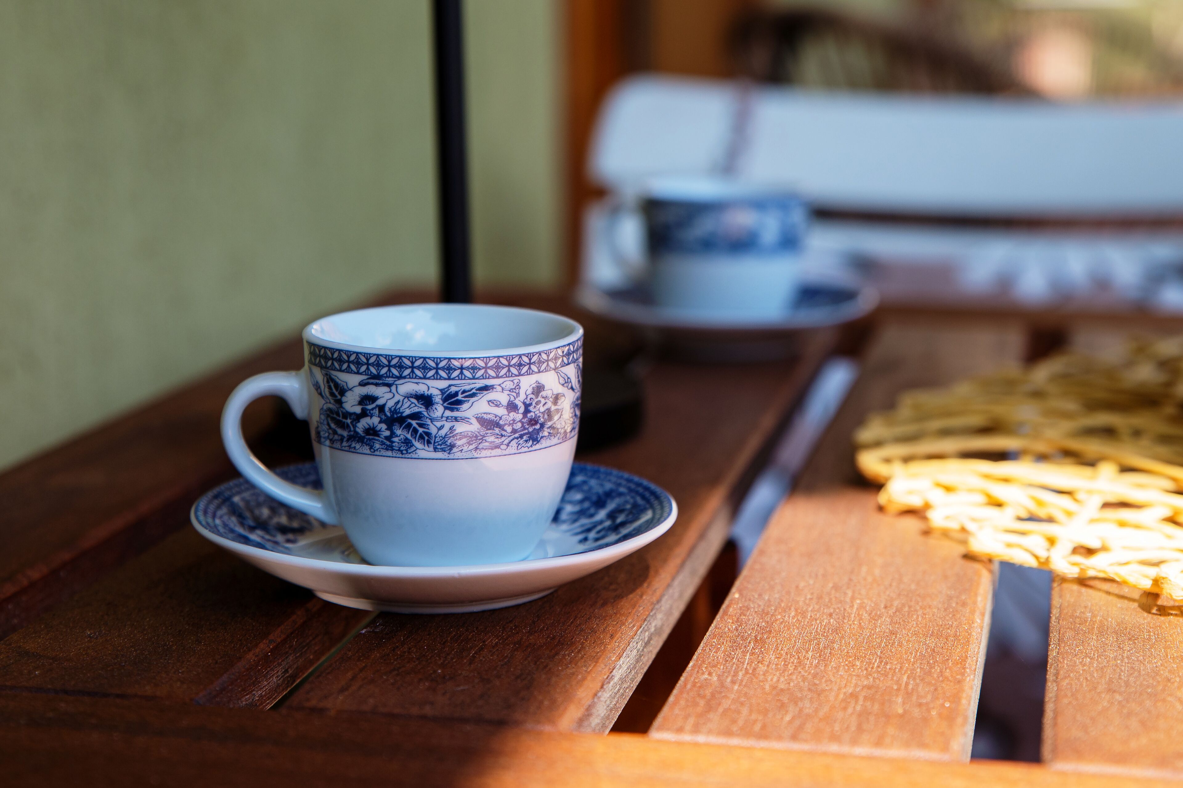Une table en bois, sur laquelle se trouvent une tasse et une soucoupe à motifs bleus et blancs, ainsi qu’une assiette de nourriture.