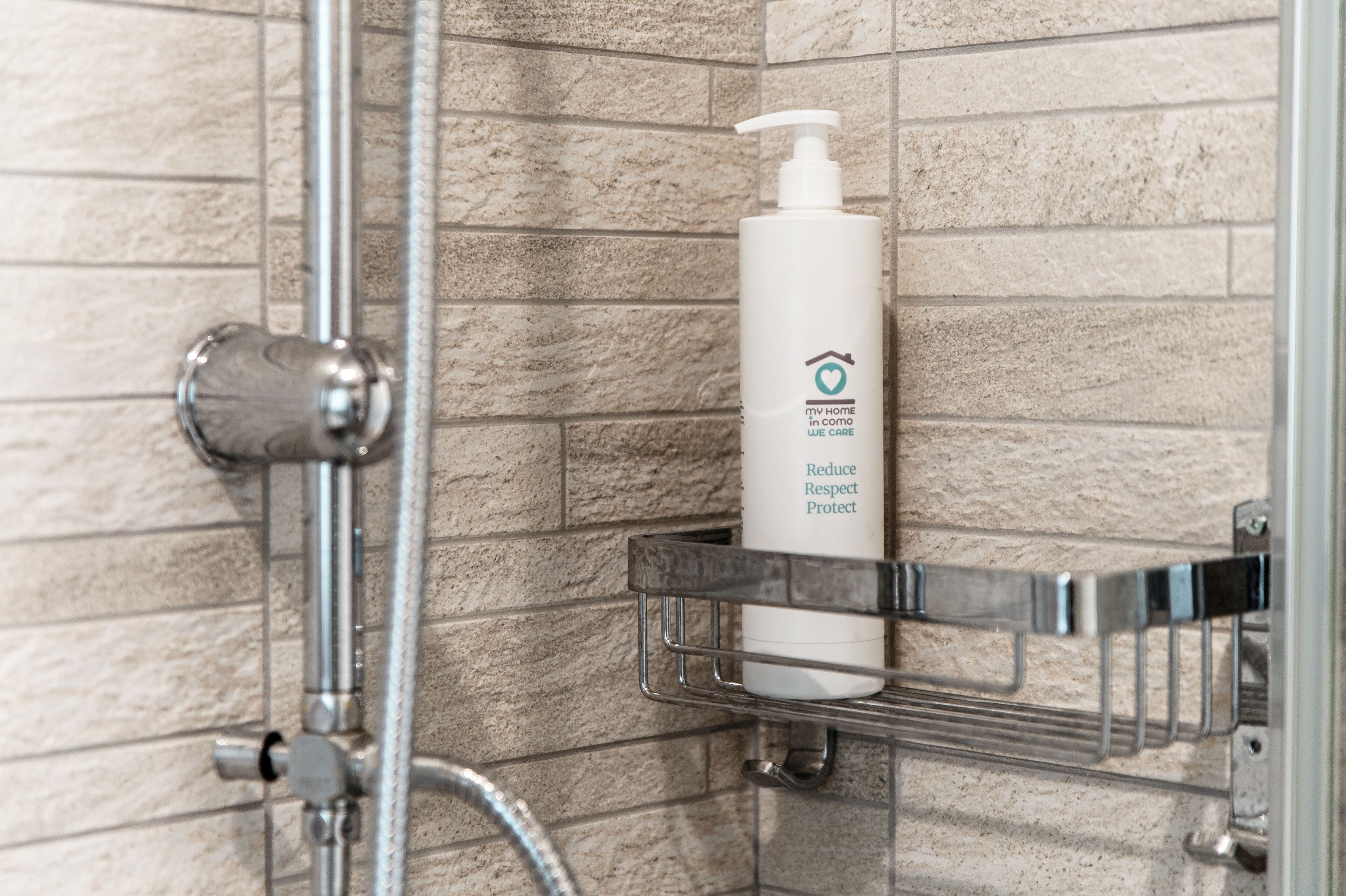 A bathroom with a shower, a hand soap dispenser on a metal shelf, and a tiled wall.