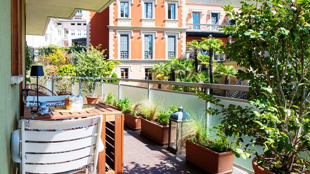 A balcony with a table, chairs, potted plants, and a view of neighboring buildings. - Cernobbio Garden View (Cernobbio)
